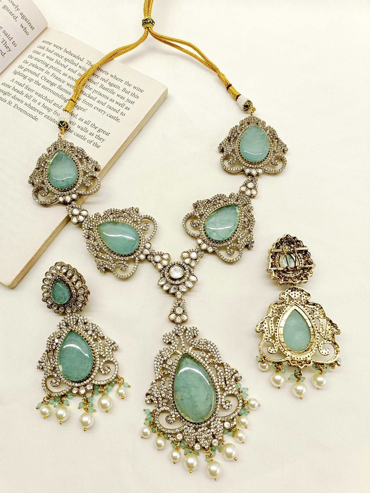 Elevate any outfit with this stunning Zakirah Aqua Blue Victorian Set, a must-have for those who appreciate the beauty of antique gold plated brass metal, American diamond setting and pearl hanging