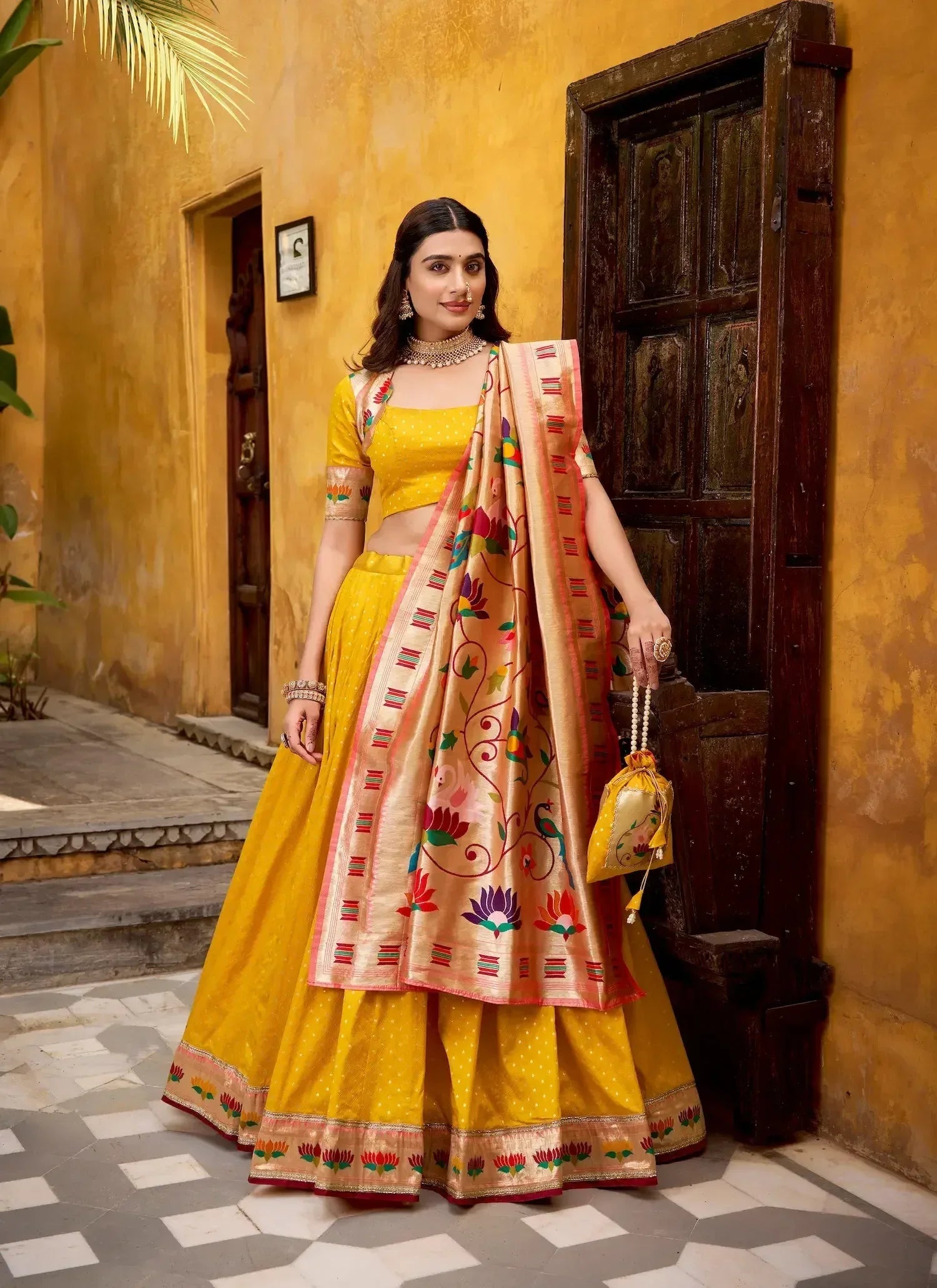 Woman in a yellow embroidered lehenga choli set with colorful dupatta, standing outdoors