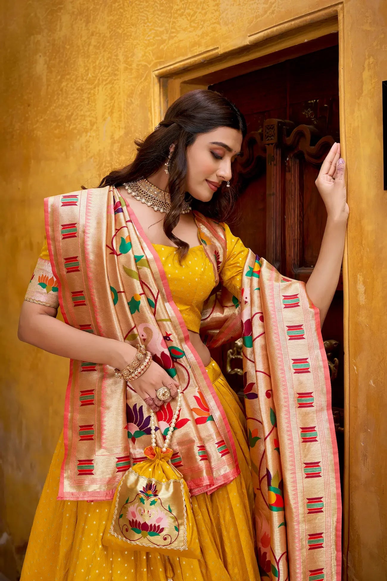 Woman in yellow traditional lehenga with embroidered dupatta and matching potli bag