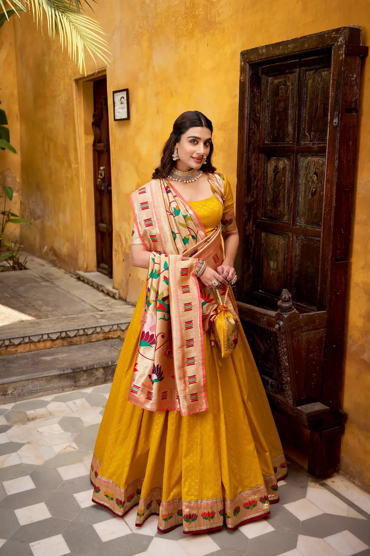 Woman in a yellow traditional lehenga with floral dupatta standing by a rustic door