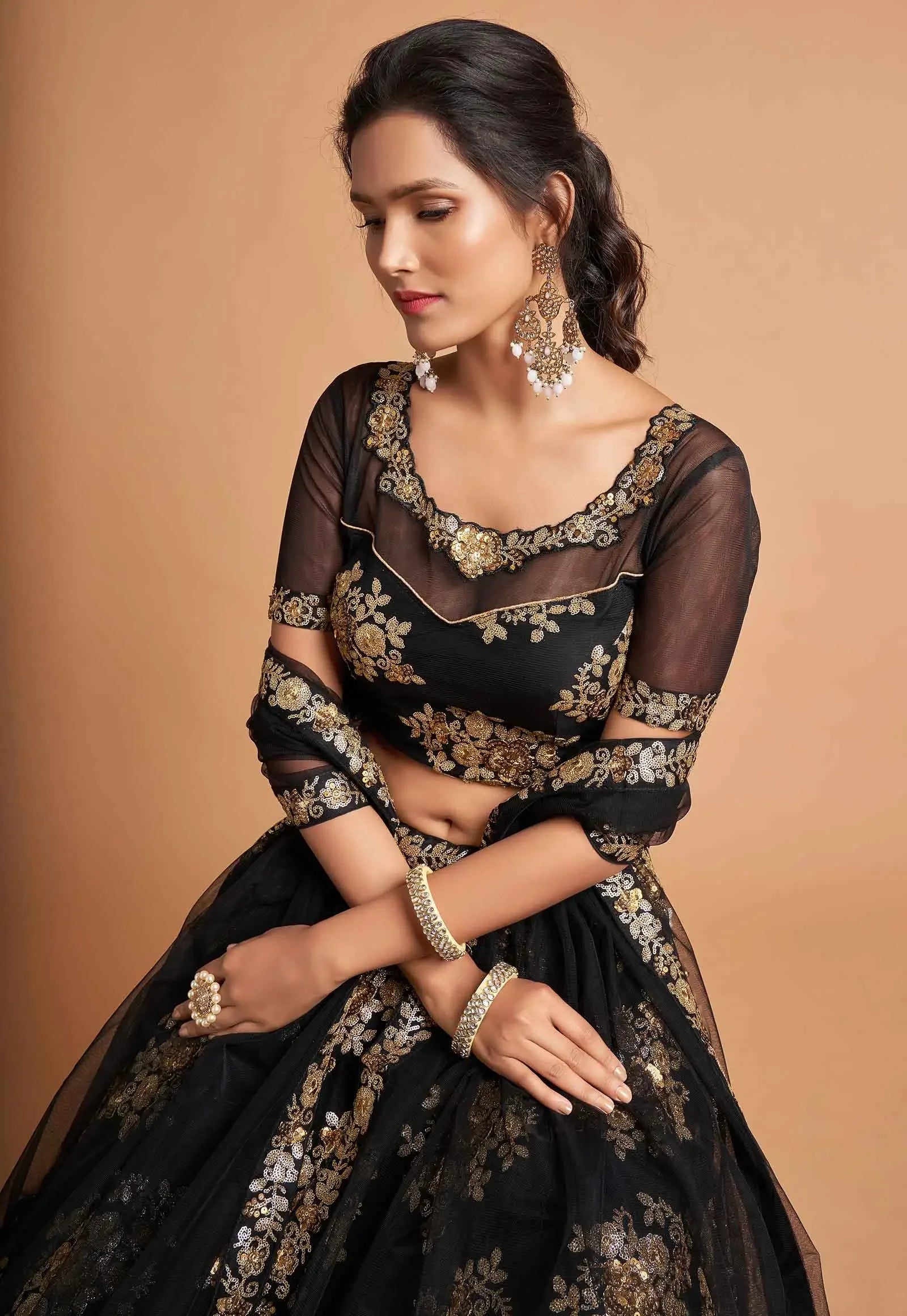 Woman wearing embroidered black and gold lehenga with sheer sleeves and ornate jewelry