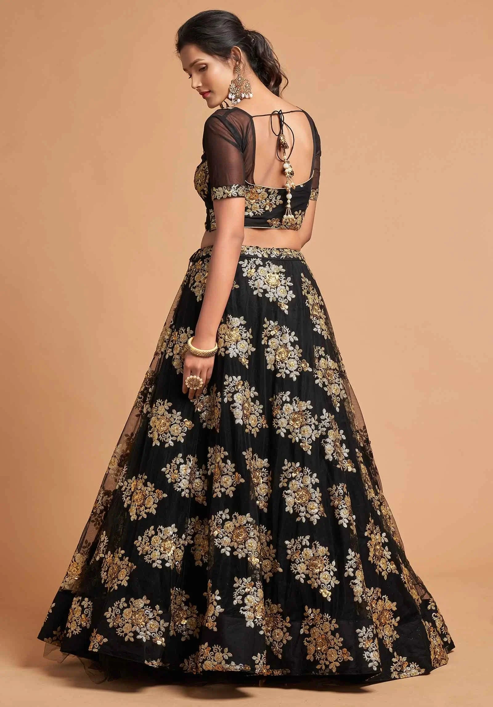 Woman in black lehenga with gold floral embroidery, sheer sleeves, and open back design
