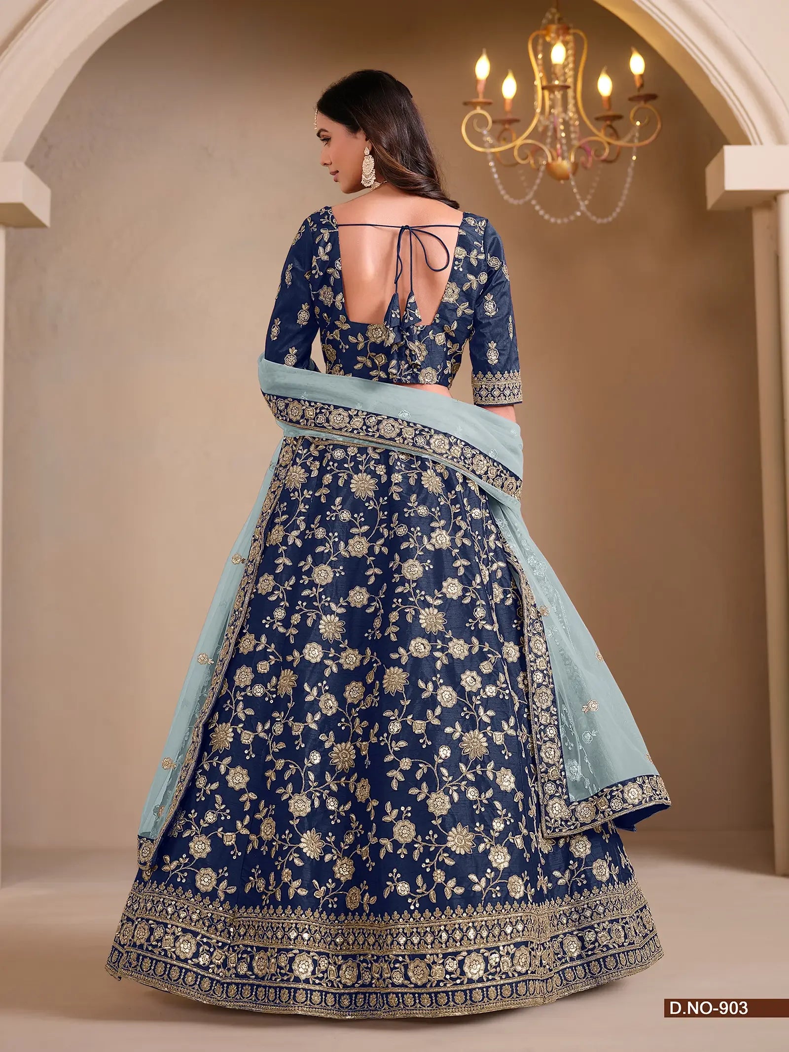 Woman wearing navy blue floral embroidered lehenga with light blue dupatta, chandelier background