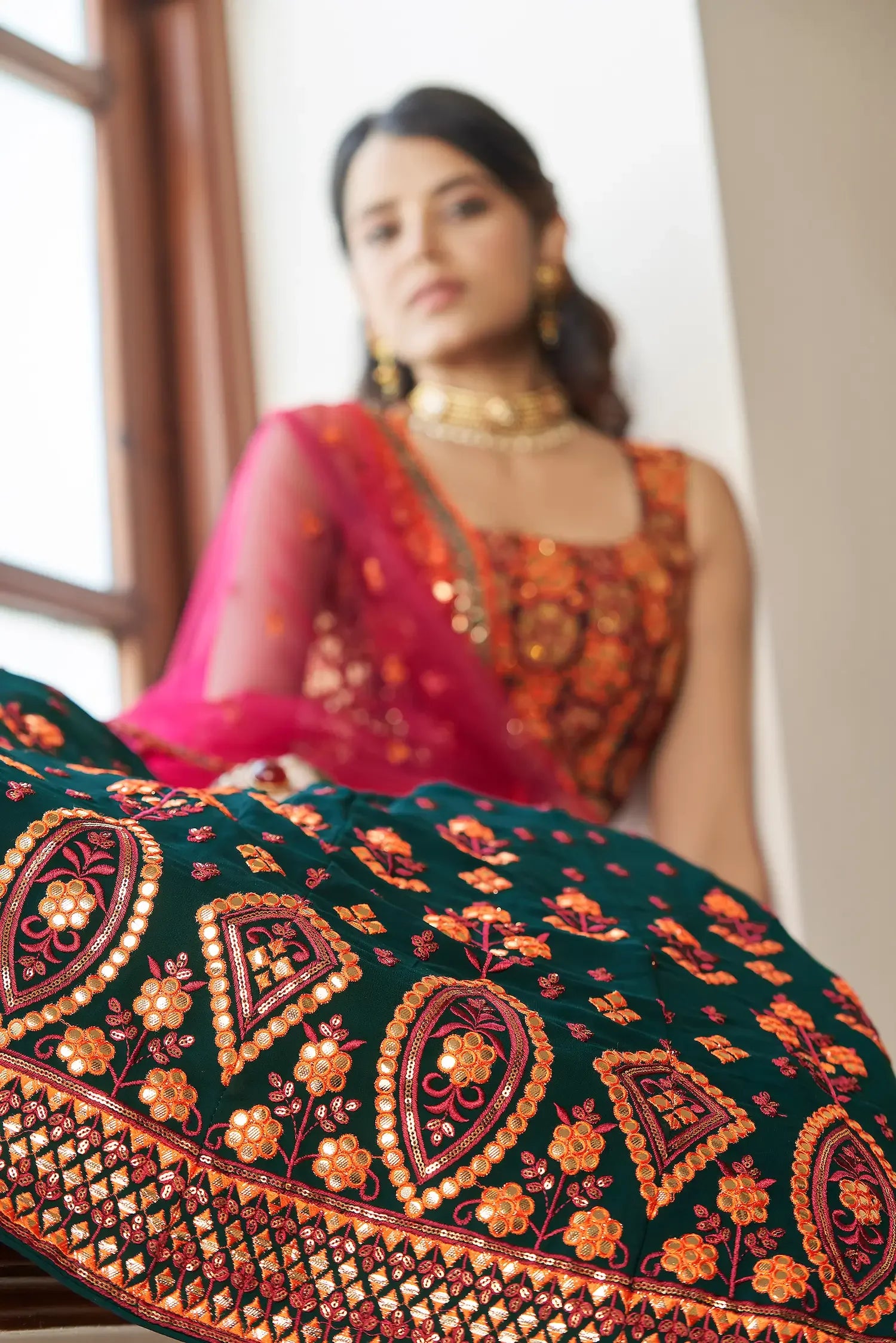 Woman wearing embroidered green and orange lehenga with floral and geometric patterns