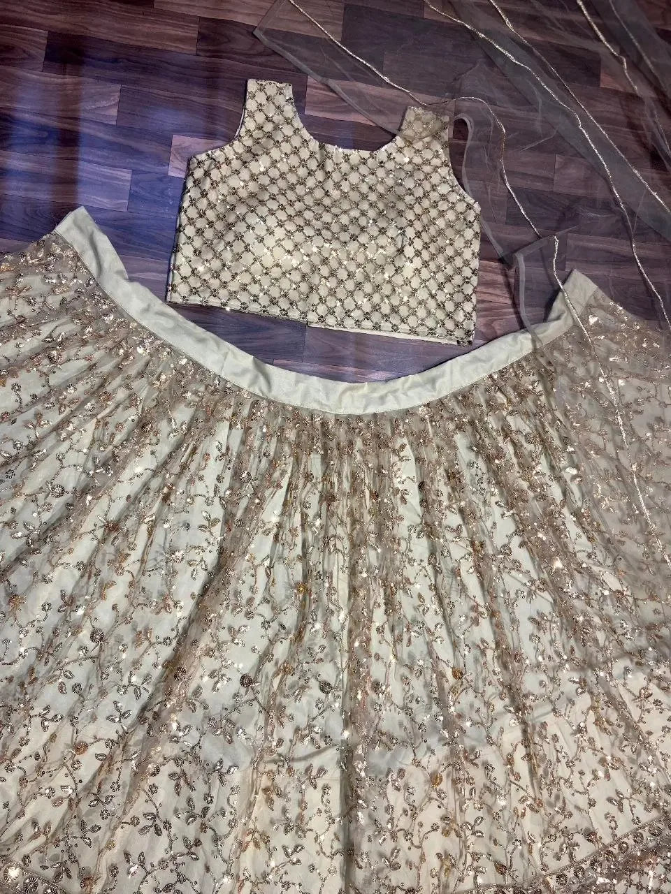 Cream and gold embroidered lehenga choli with sequin work on wooden floor