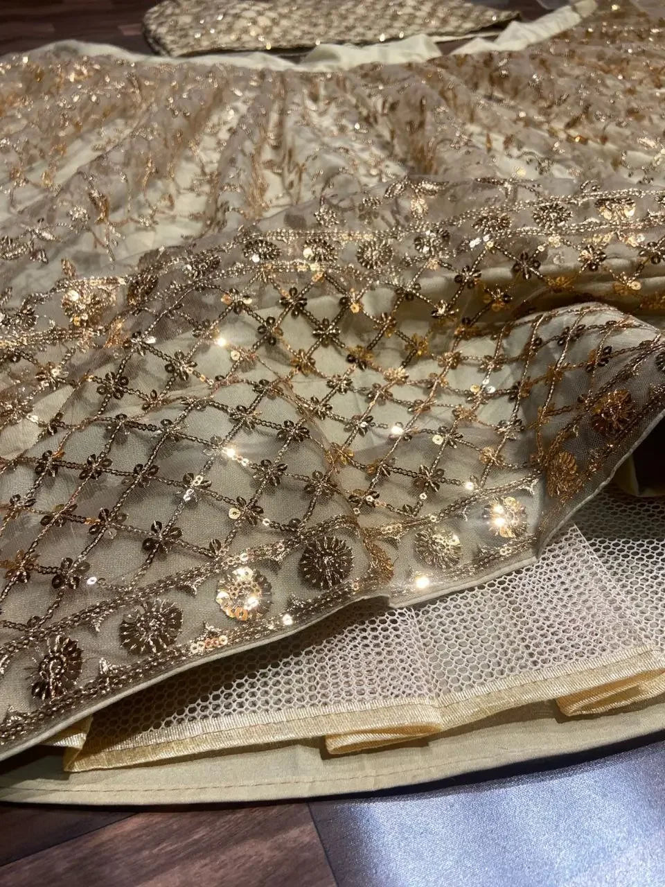 Gold sequin embroidered net fabric with floral and lattice patterns on cream lining