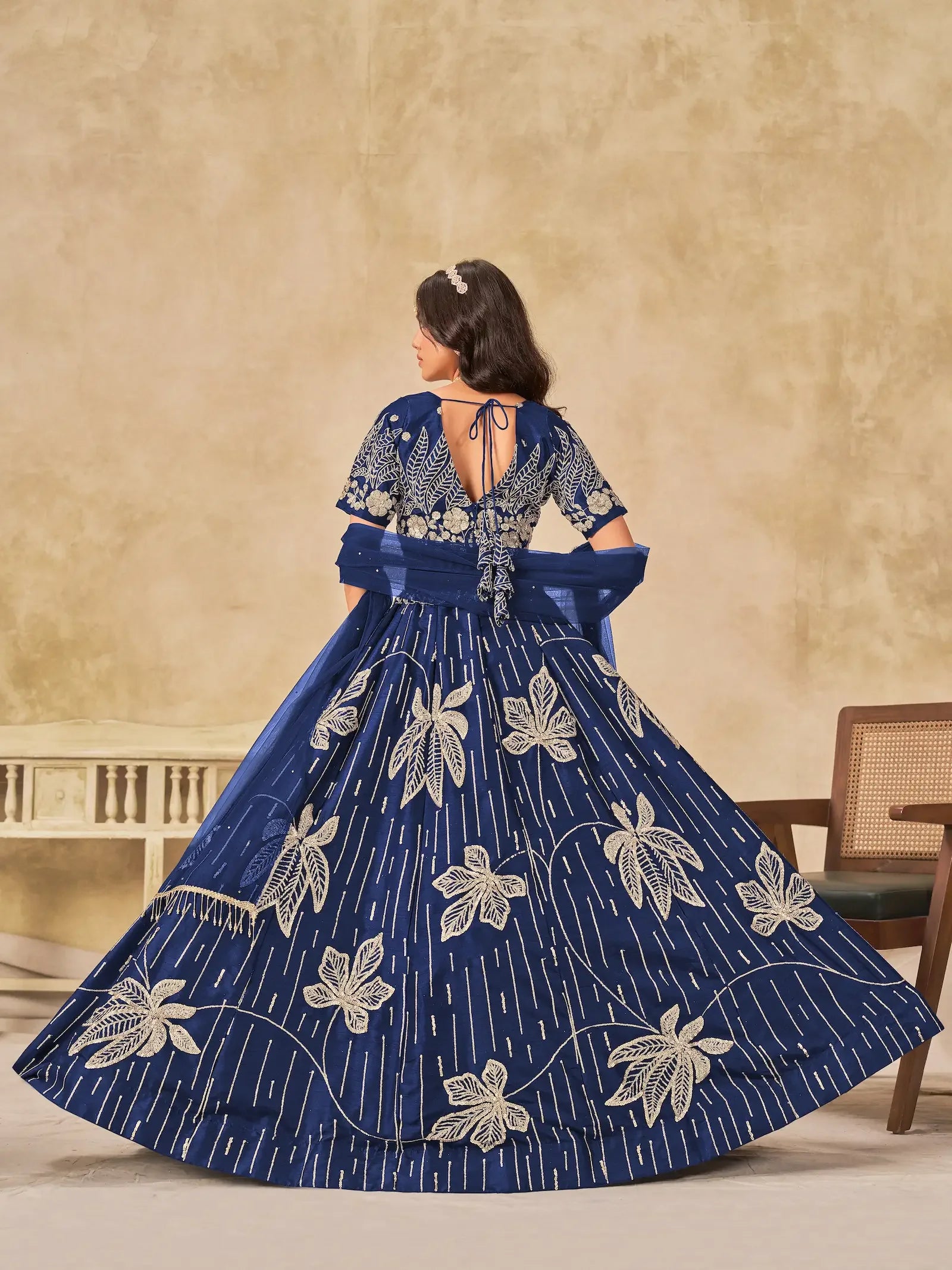 Woman in a blue embroidered gown with floral patterns and open back, indoor setting