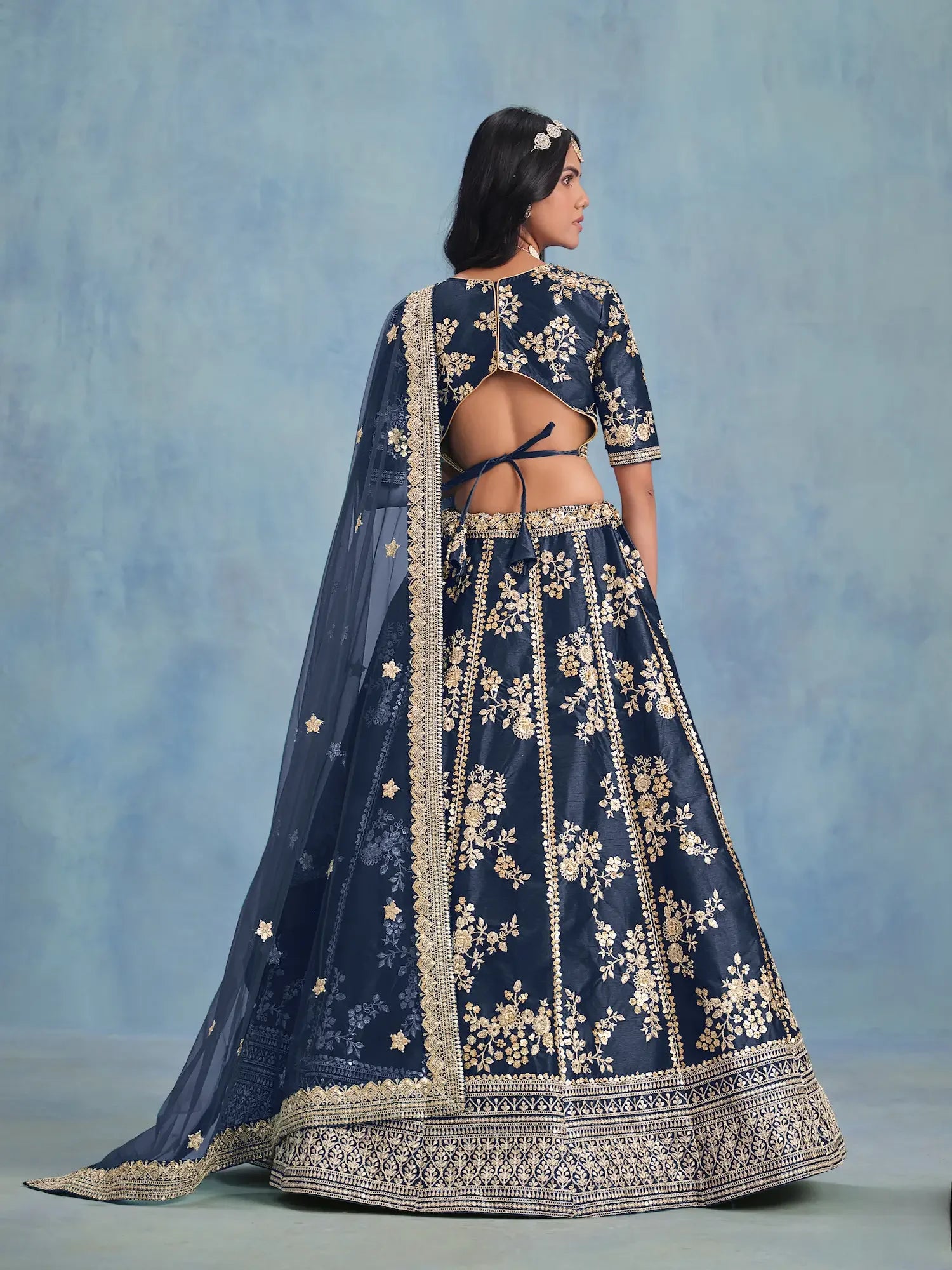 Woman wearing navy blue embroidered lehenga with gold floral patterns, open-back blouse, dupatta