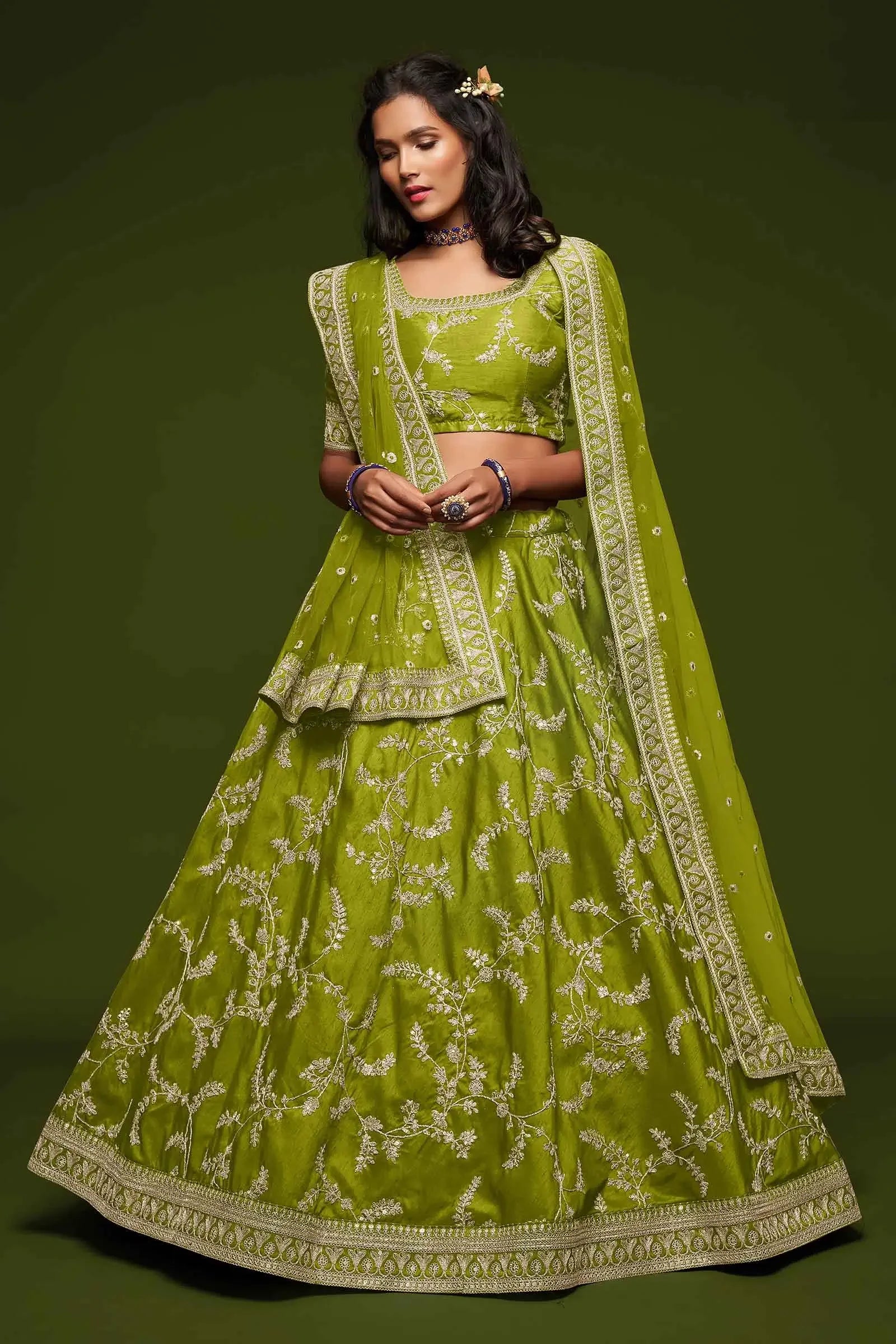 Woman wearing lime green embroidered lehenga choli with dupatta on green background
