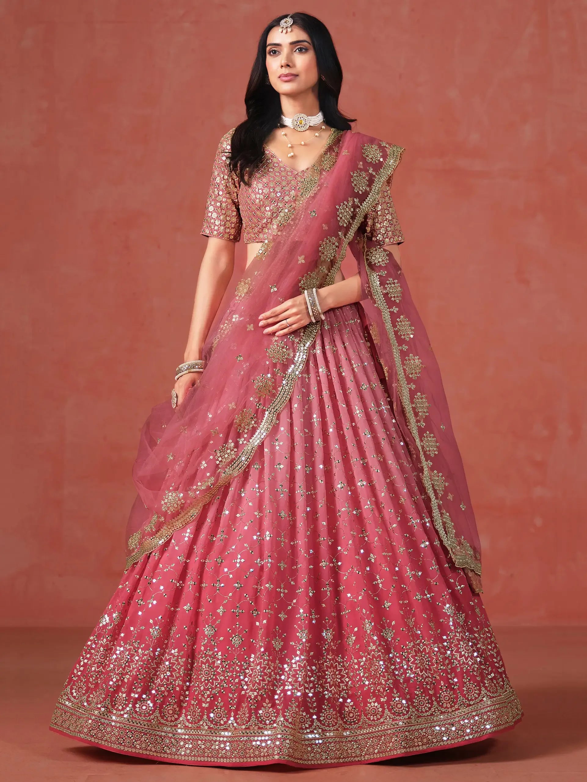 Woman in a pink and gold embellished lehenga with matching dupatta, traditional jewelry