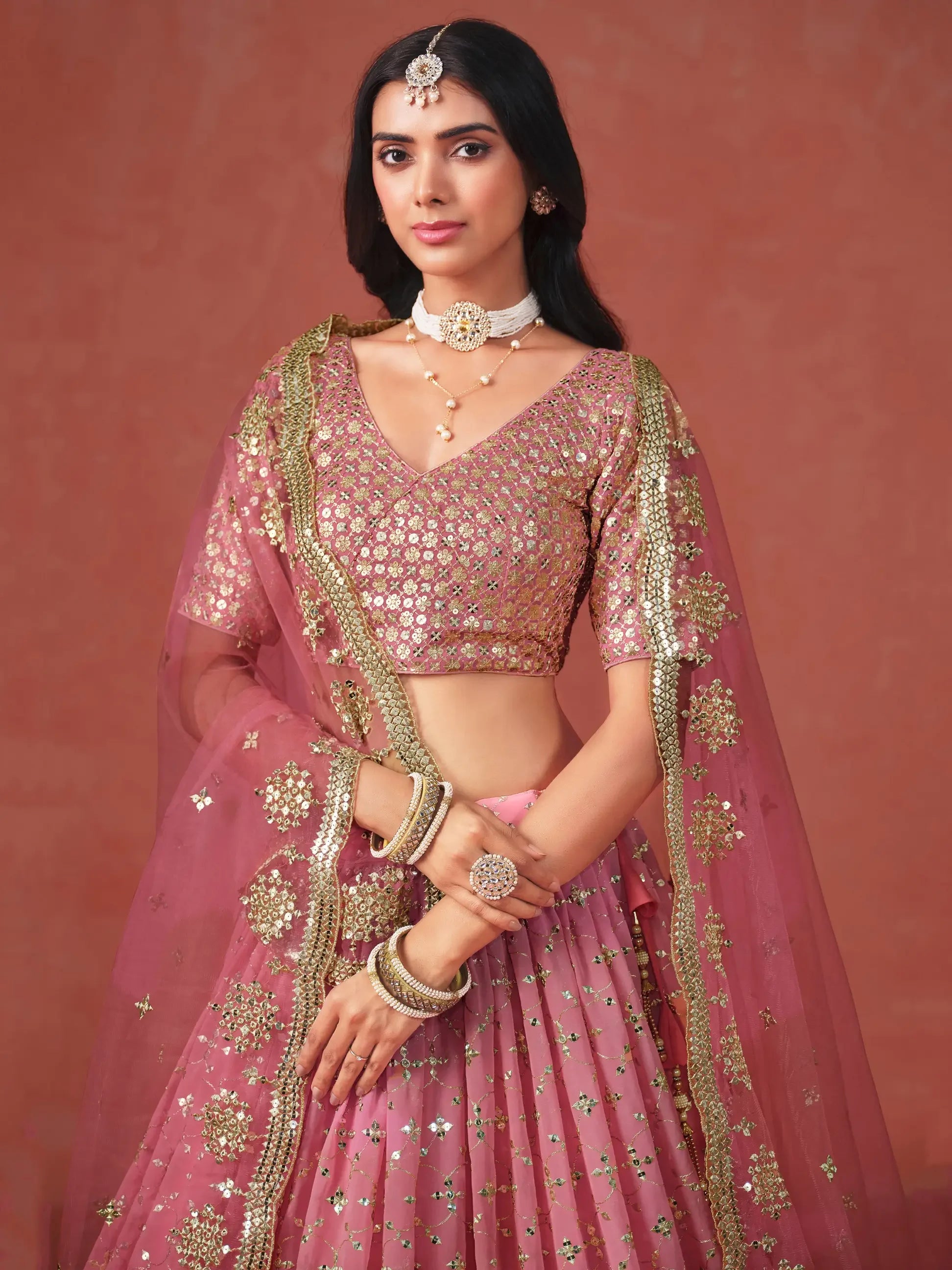 Woman wearing pink embroidered lehenga choli with gold accents and traditional jewelry