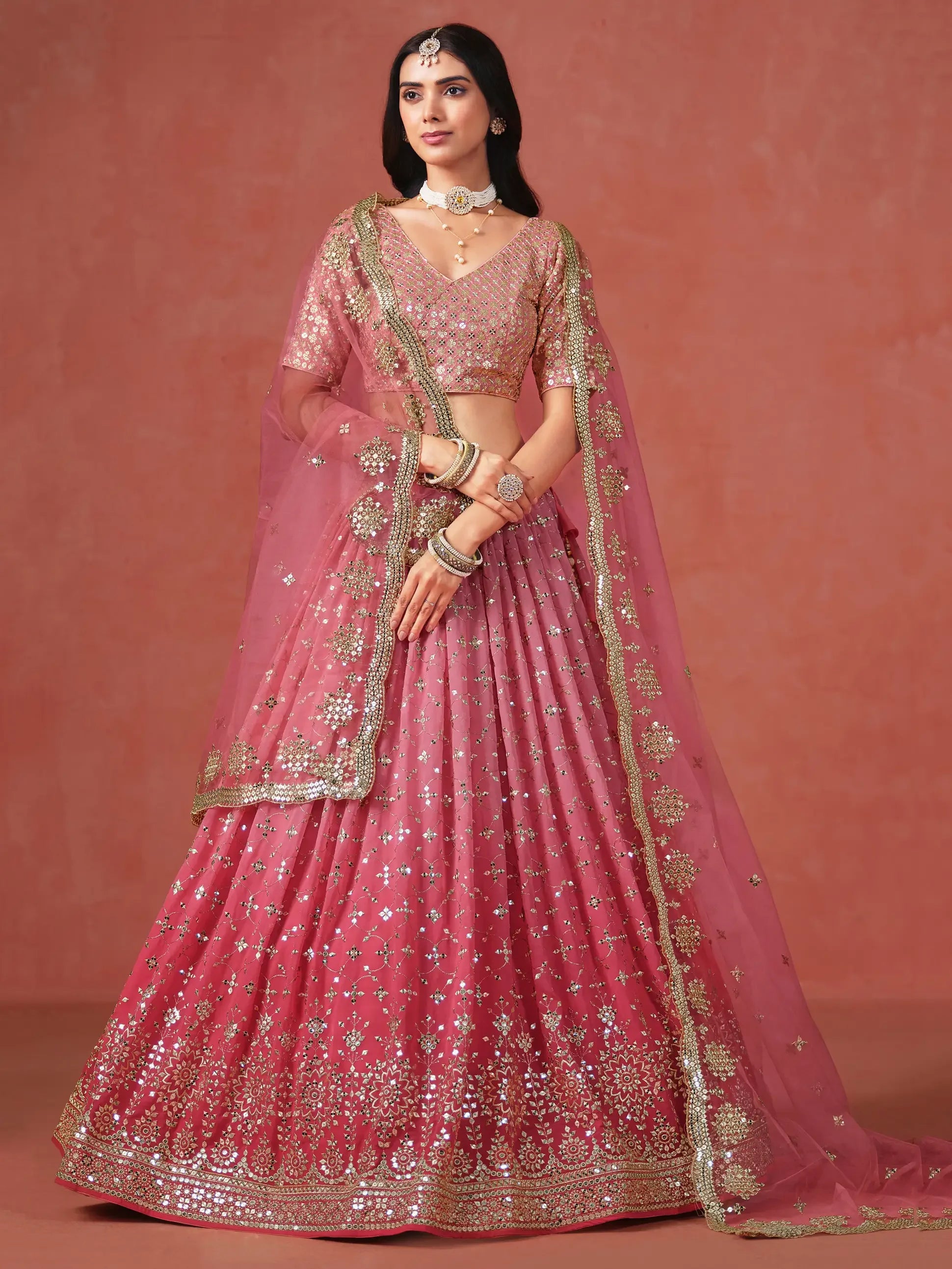 Woman in pink and gold embroidered lehenga choli with dupatta, traditional Indian attire