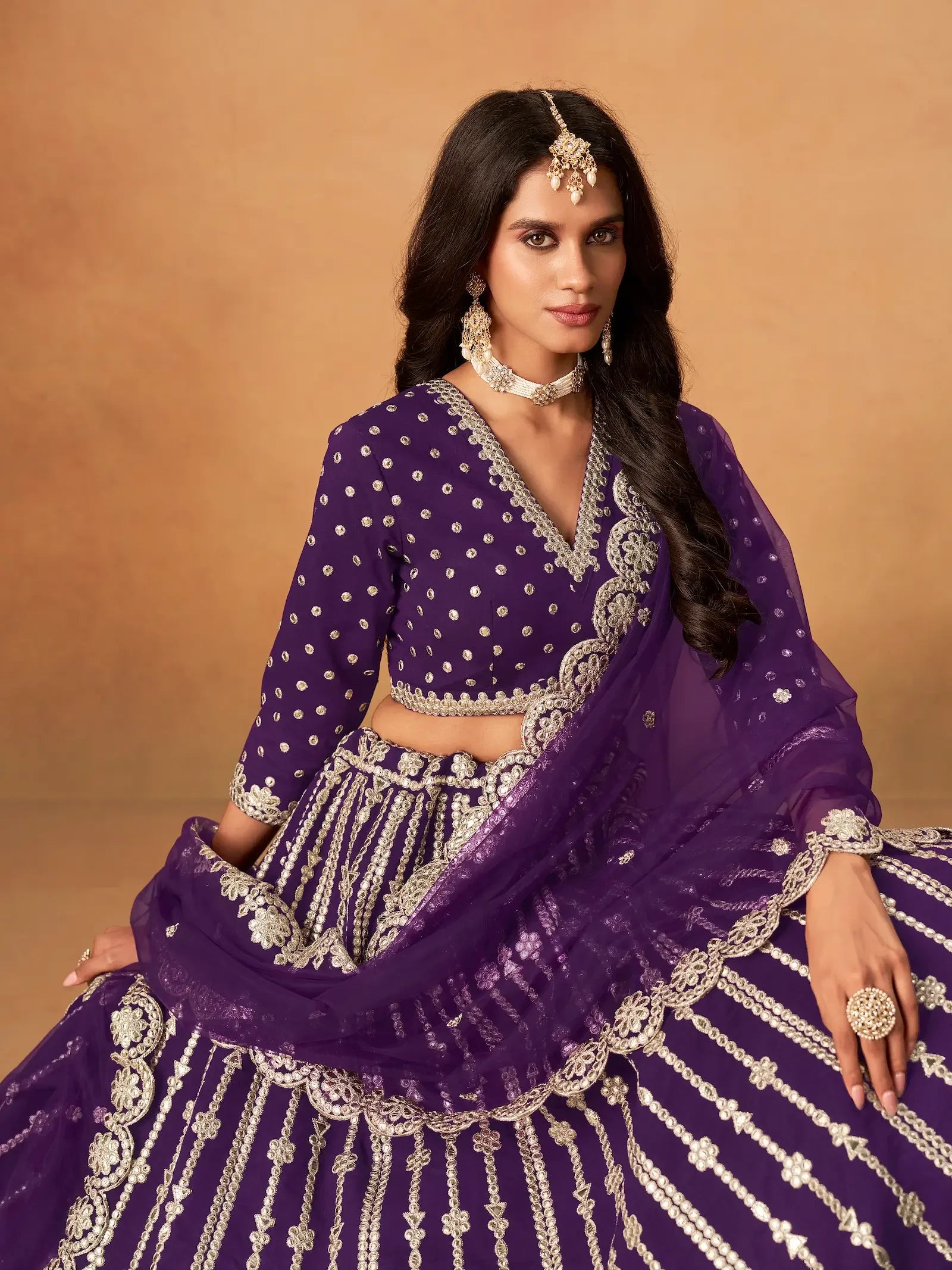 Woman in purple embroidered lehenga choli with silver jewelry on beige background
