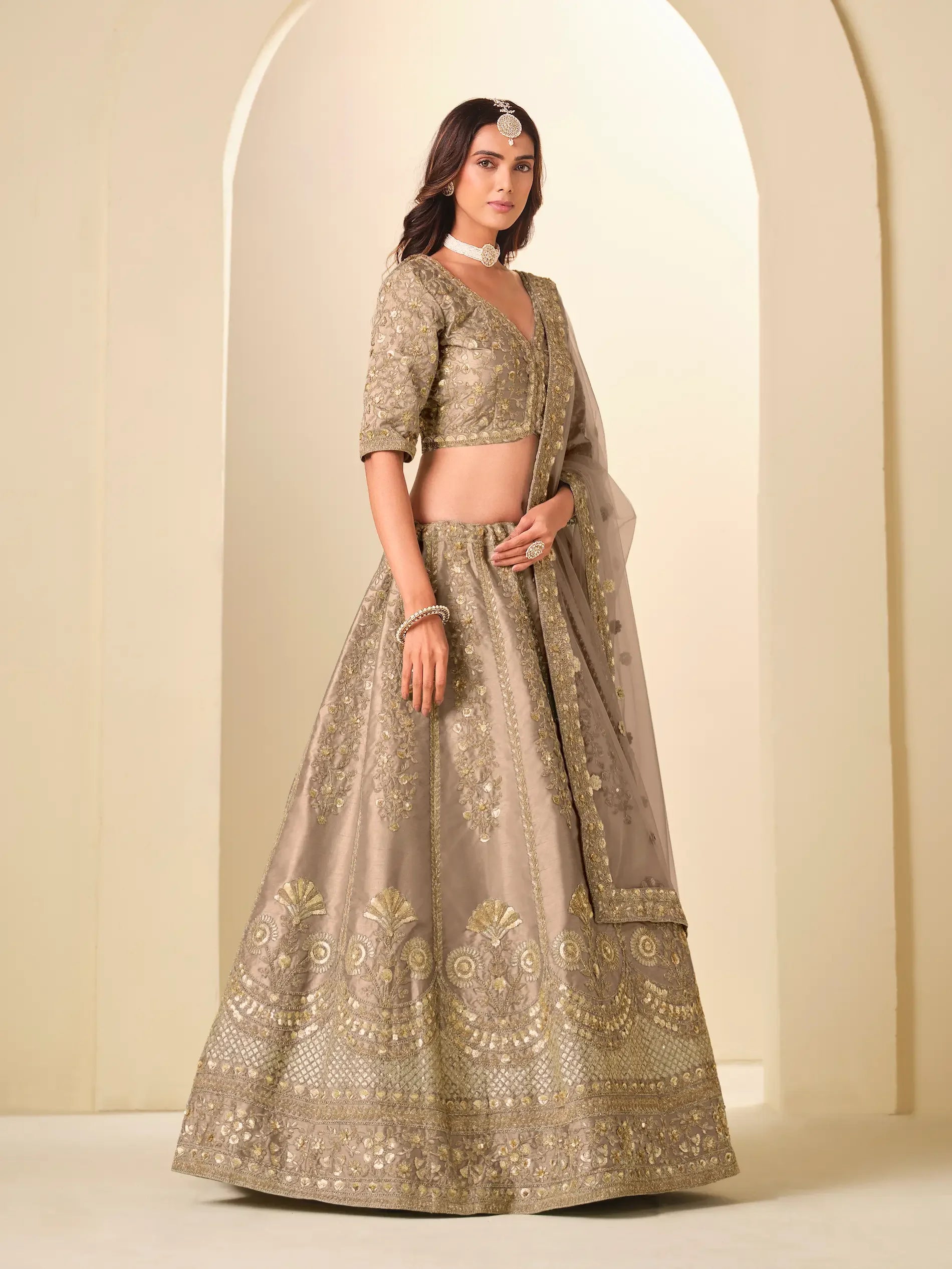 Woman wearing an embroidered beige lehenga choli with matching dupatta and traditional jewelry