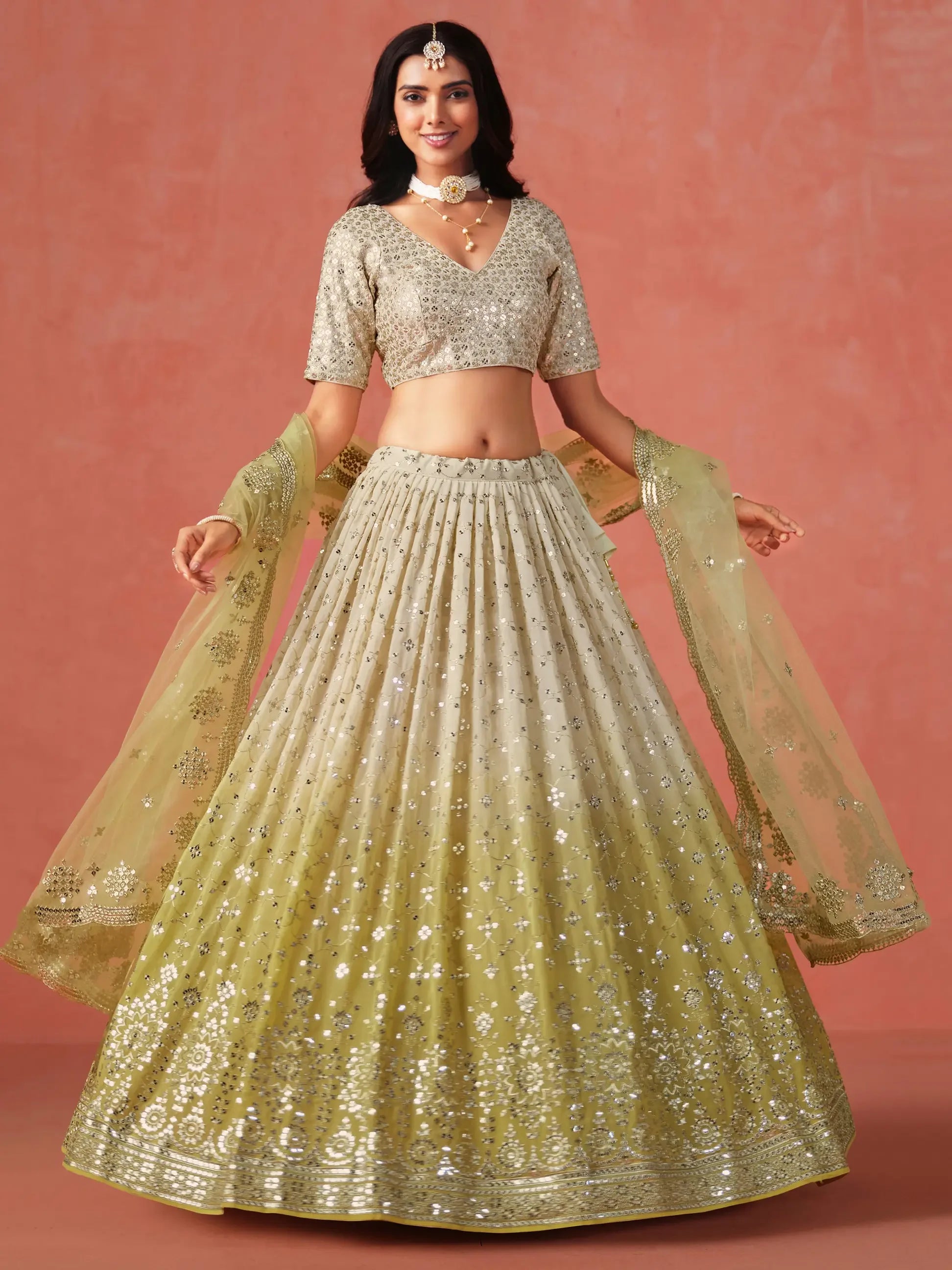 Woman in gold embroidered lehenga choli with sheer dupatta and jewelry, standing indoors