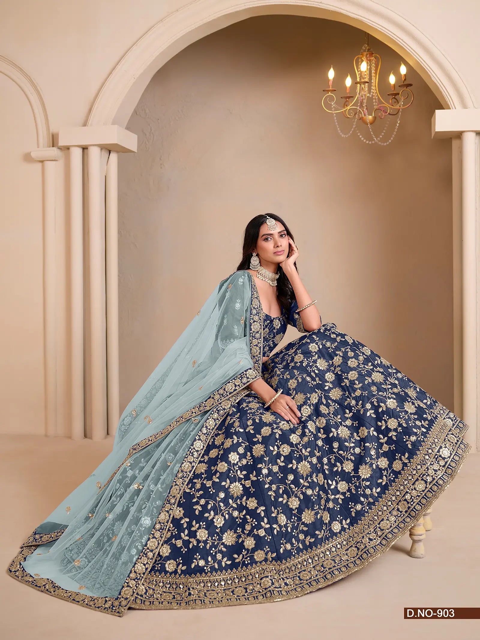 Woman wearing navy blue and gold embroidered lehenga with light blue dupatta, elegant indoor setting