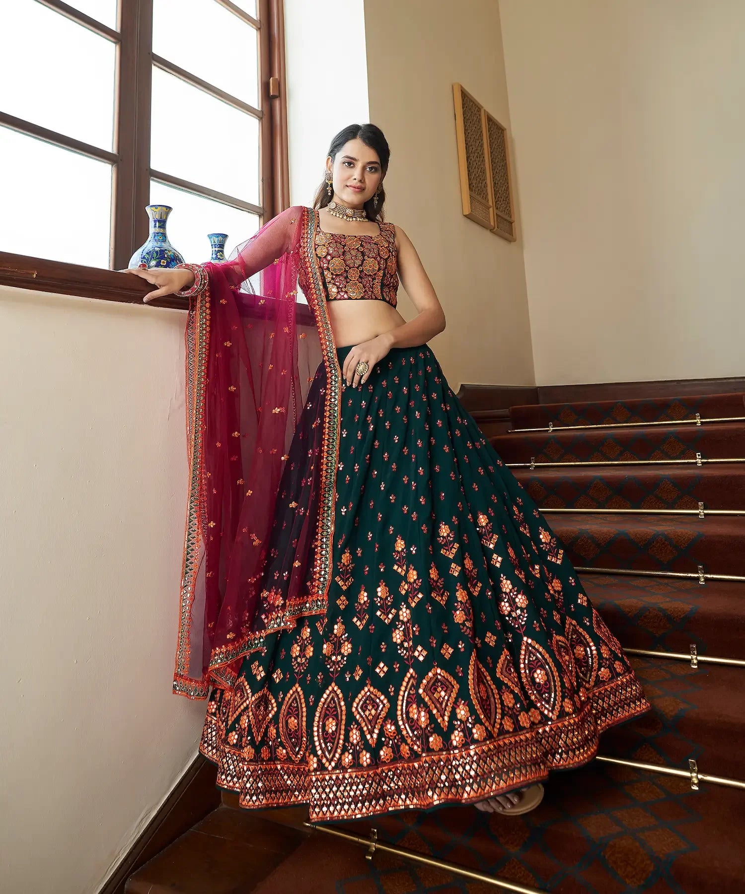 Woman in a traditional green and maroon embroidered lehenga with dupatta on staircase