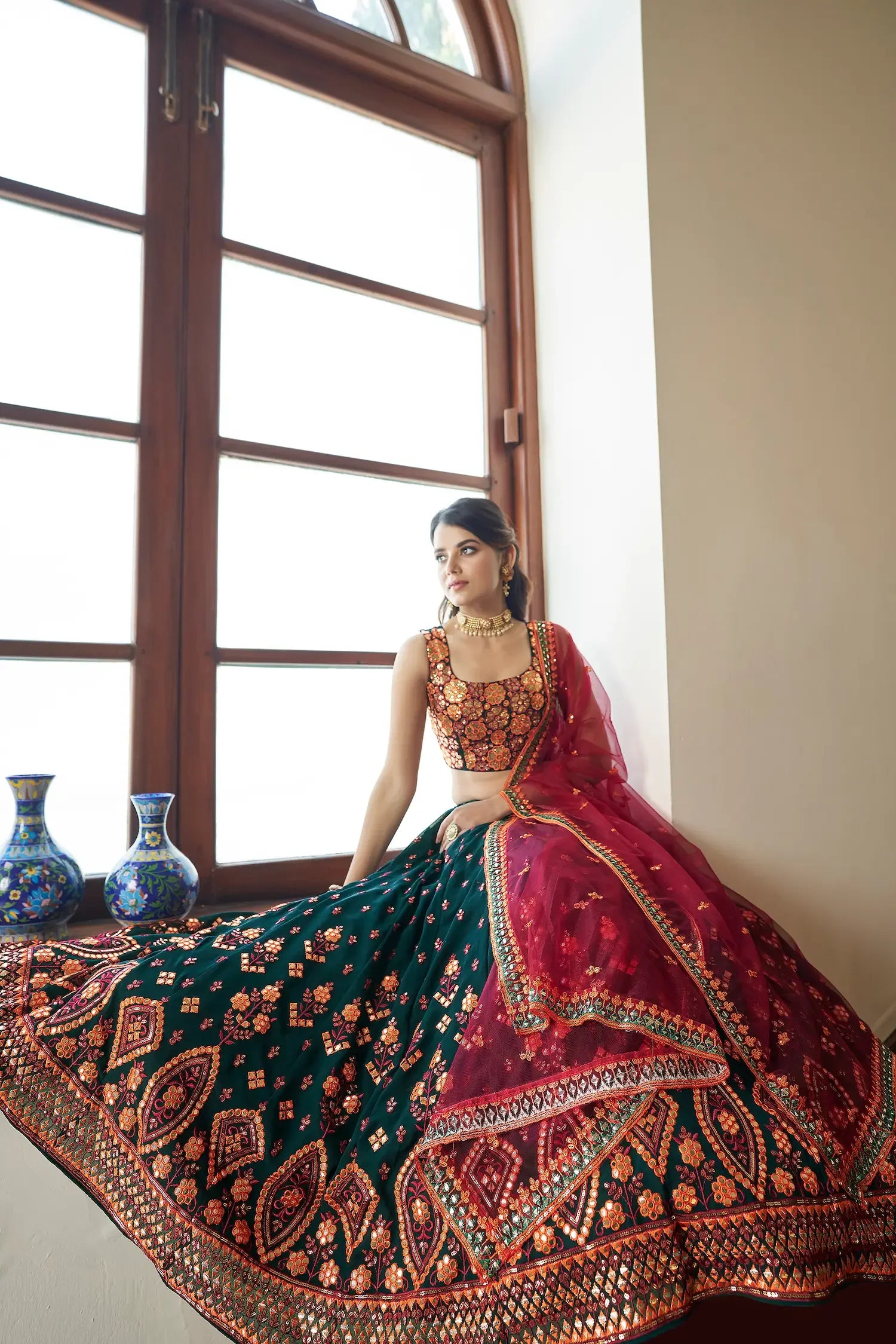 Woman in traditional embroidered lehenga with maroon dupatta by a window