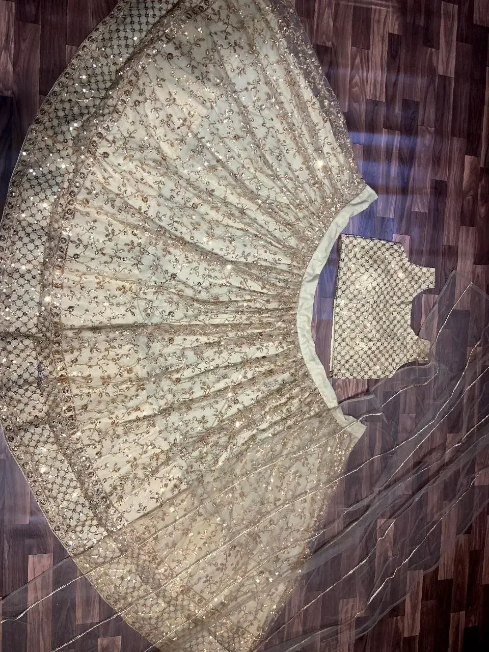 Ivory and gold embroidered lehenga with matching blouse and dupatta on wooden floor