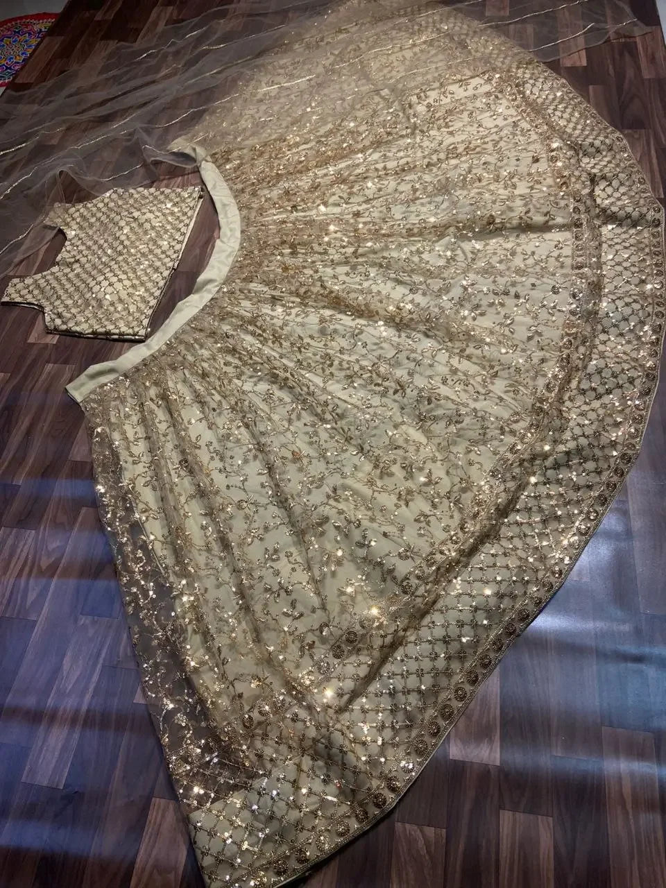 Gold embroidered lehenga choli with sequin work and matching dupatta on wooden floor