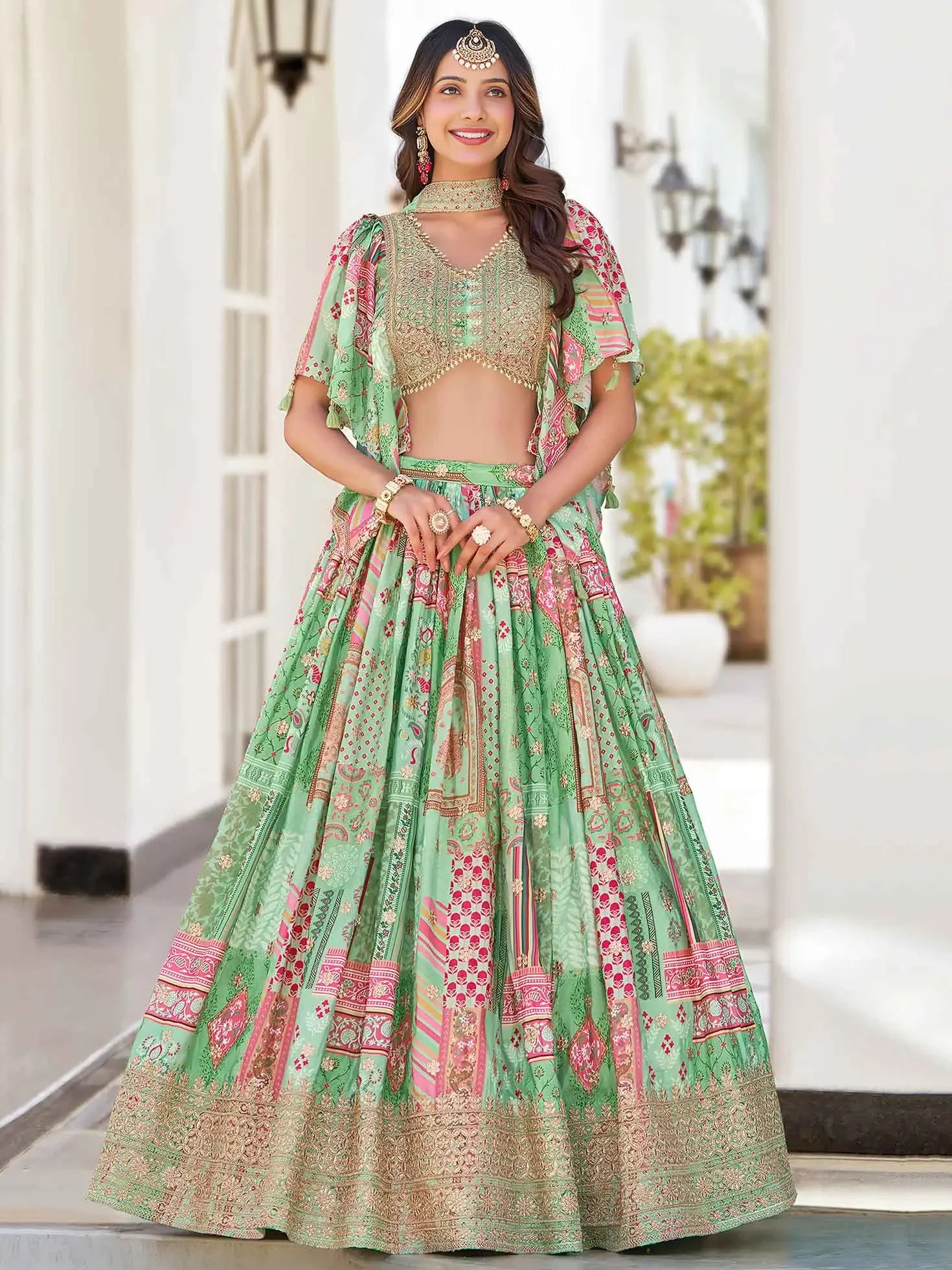 Woman wearing a green and pink lehenga choli with gold embroidery, standing in a hallway