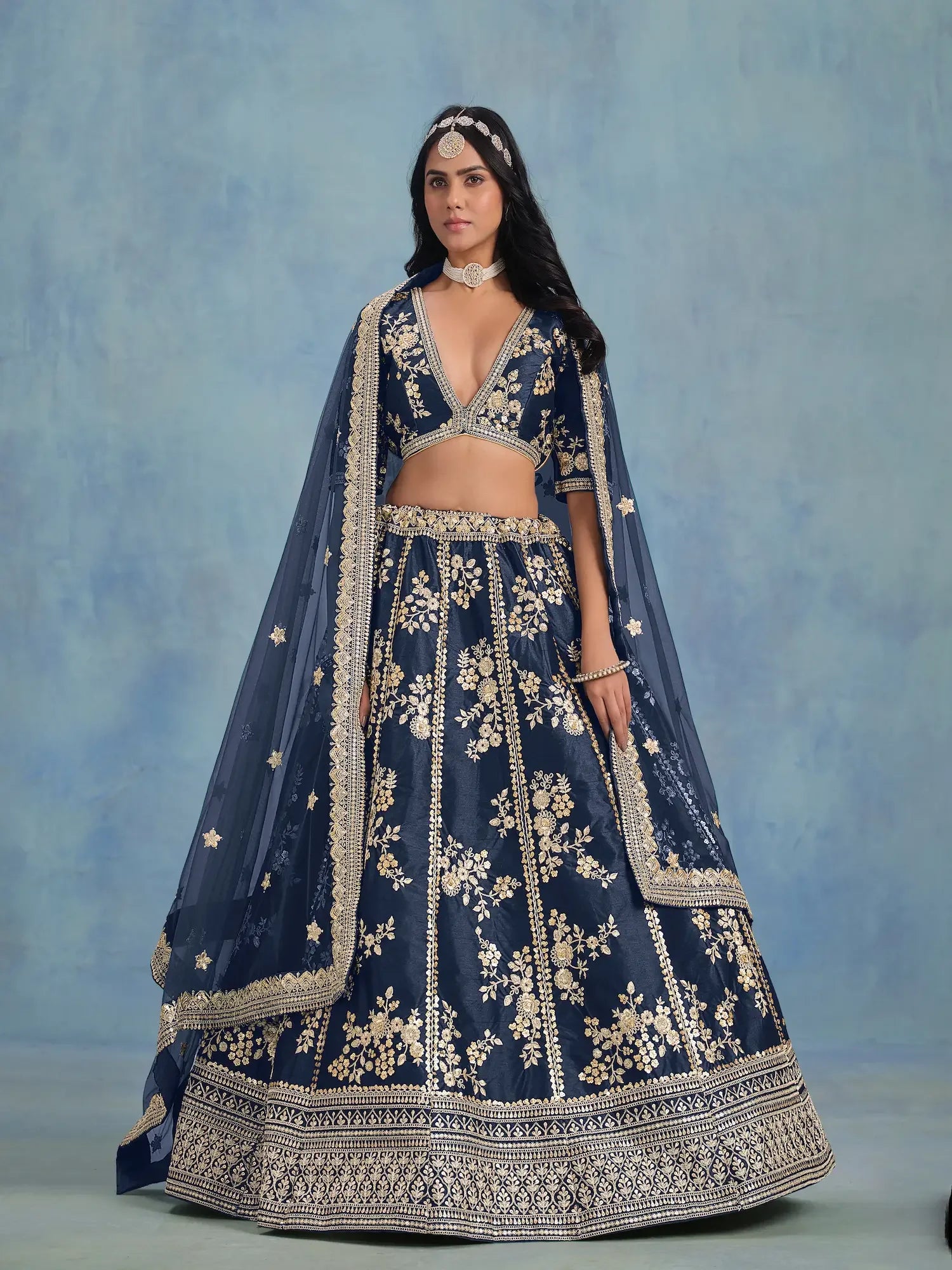 Woman wearing navy blue embroidered lehenga with gold floral patterns and matching dupatta
