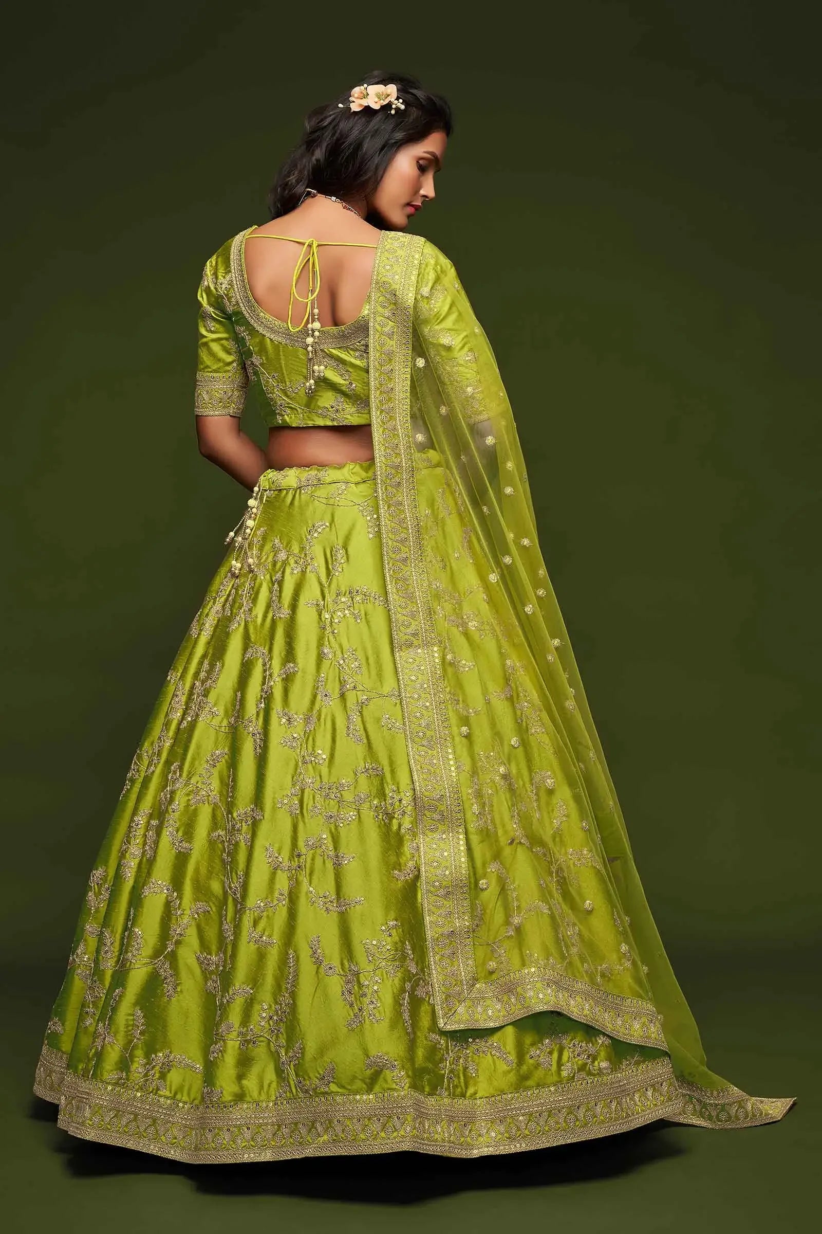 Woman wearing backless lime green embroidered lehenga with dupatta, floral hair accessory