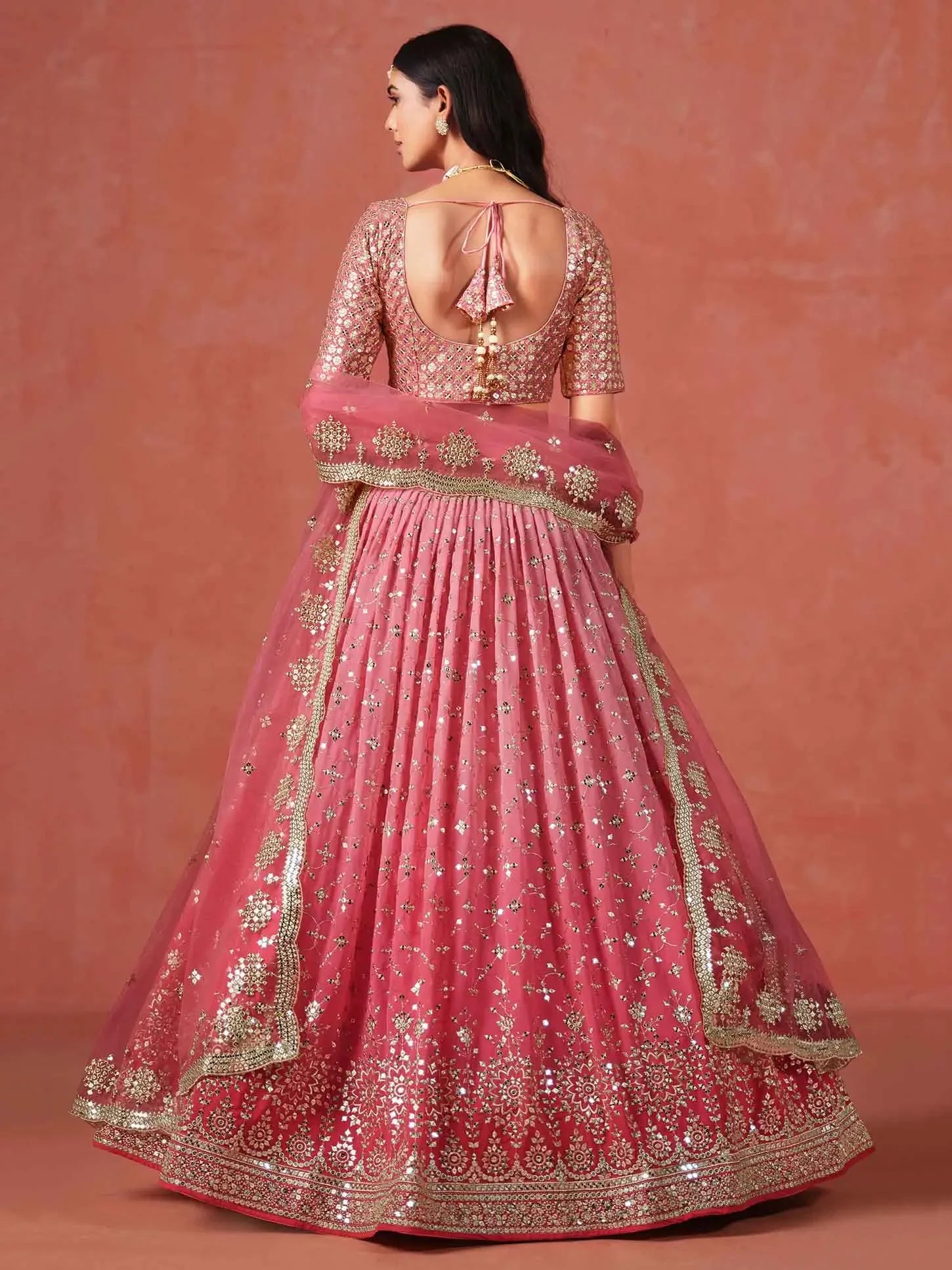 Woman in pink embroidered lehenga with open-back blouse and dupatta, traditional attire