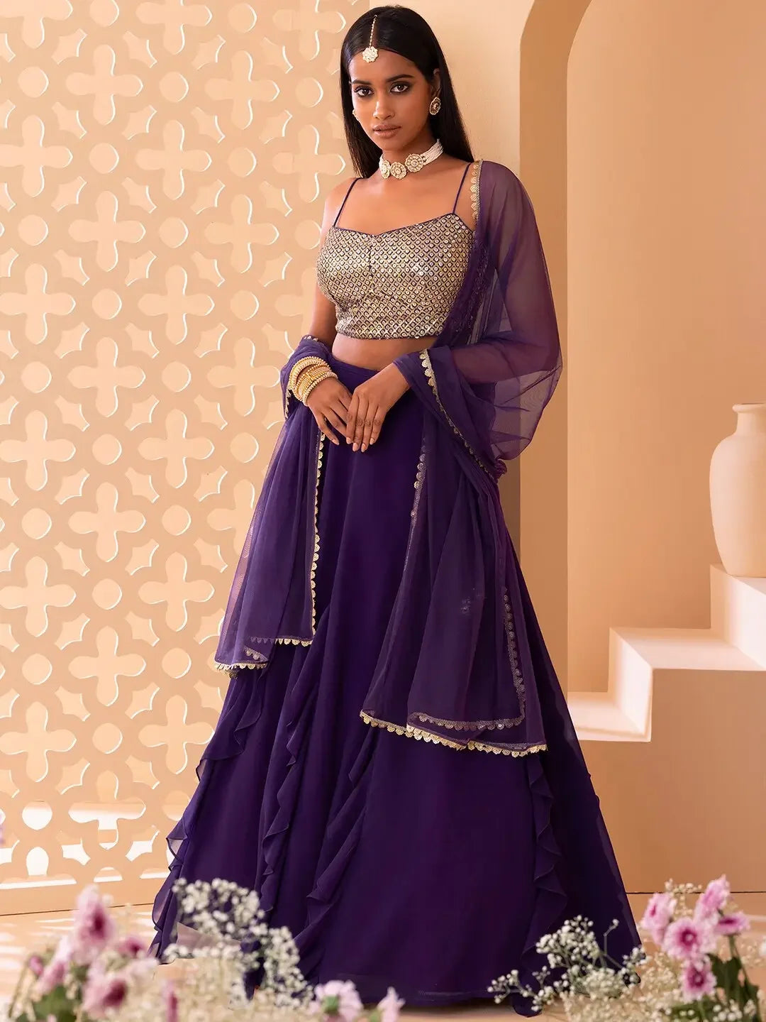 Woman wearing a purple embellished lehenga with dupatta, gold jewelry, floral decor