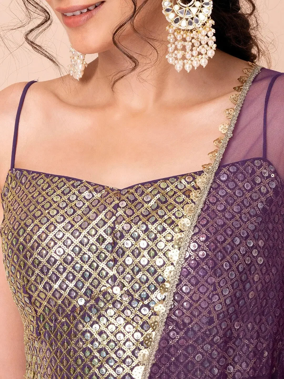 Woman wearing a purple sequin embroidered saree with gold accents and statement earrings