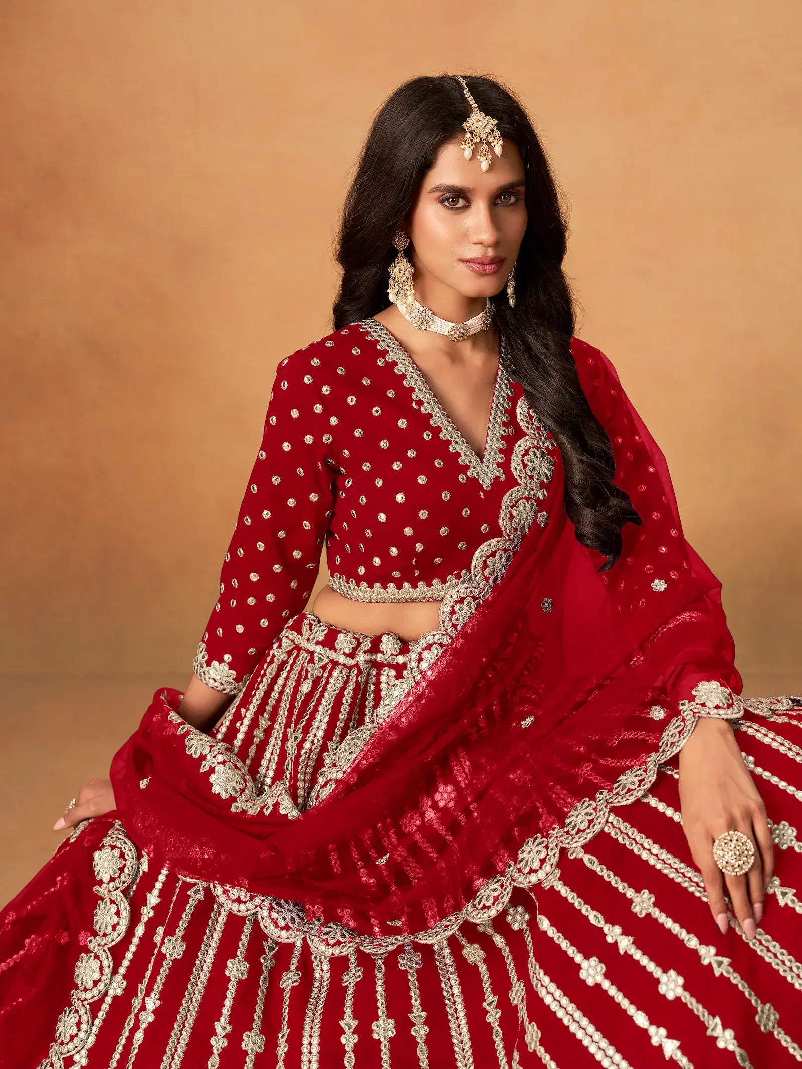 Woman wearing traditional red and silver embroidered lehenga with jewelry on beige background
