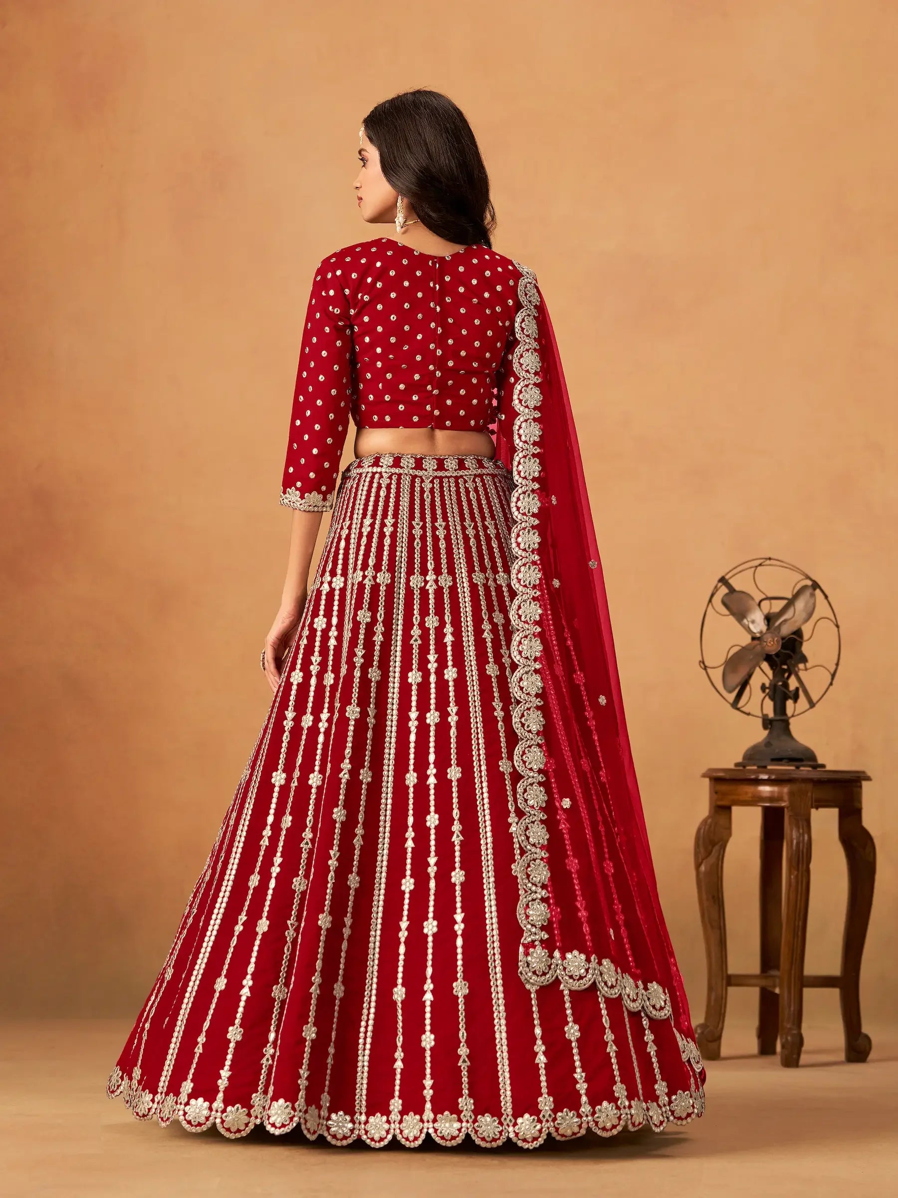 Woman in red embroidered lehenga set with silver details, traditional attire, neutral backdrop