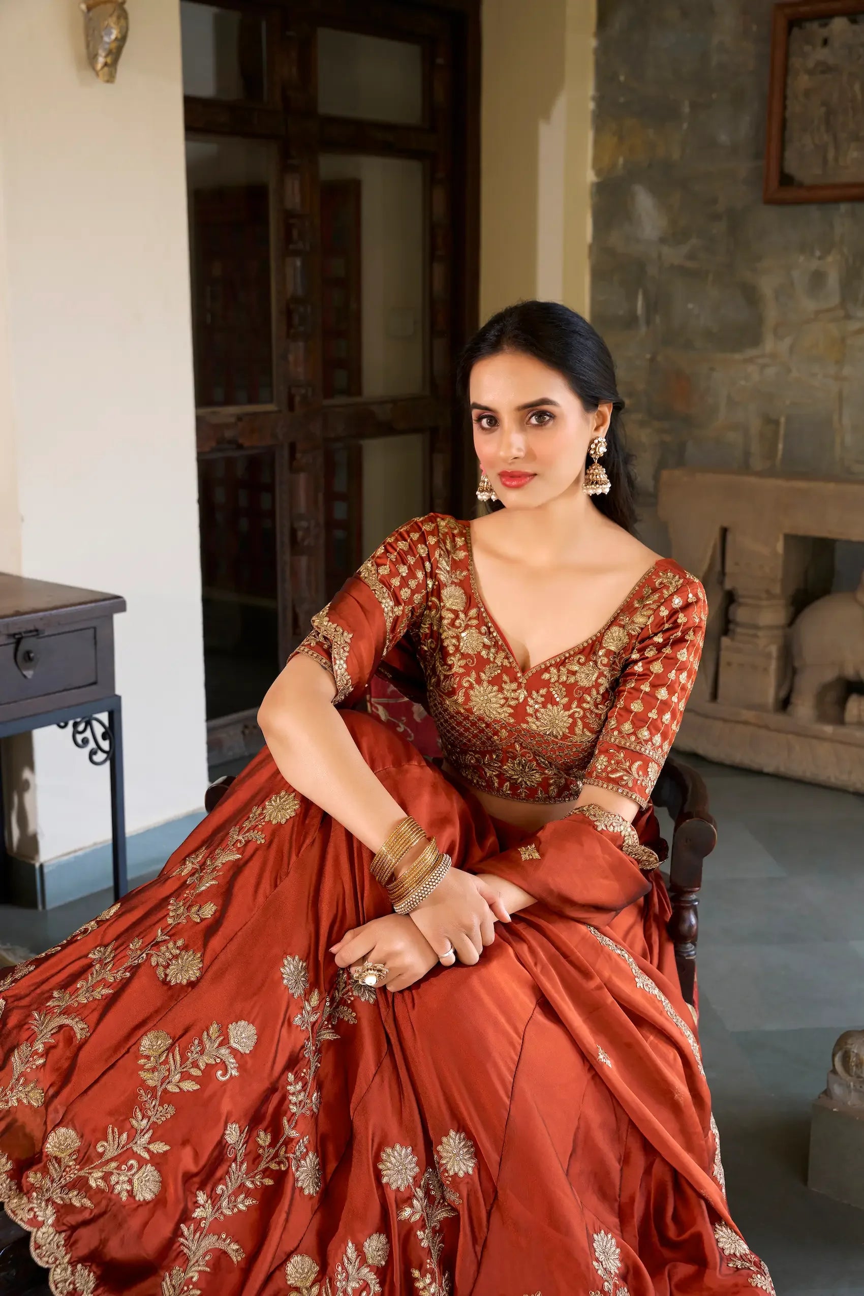 Woman in an embroidered rust orange lehenga with gold floral patterns, traditional jewelry