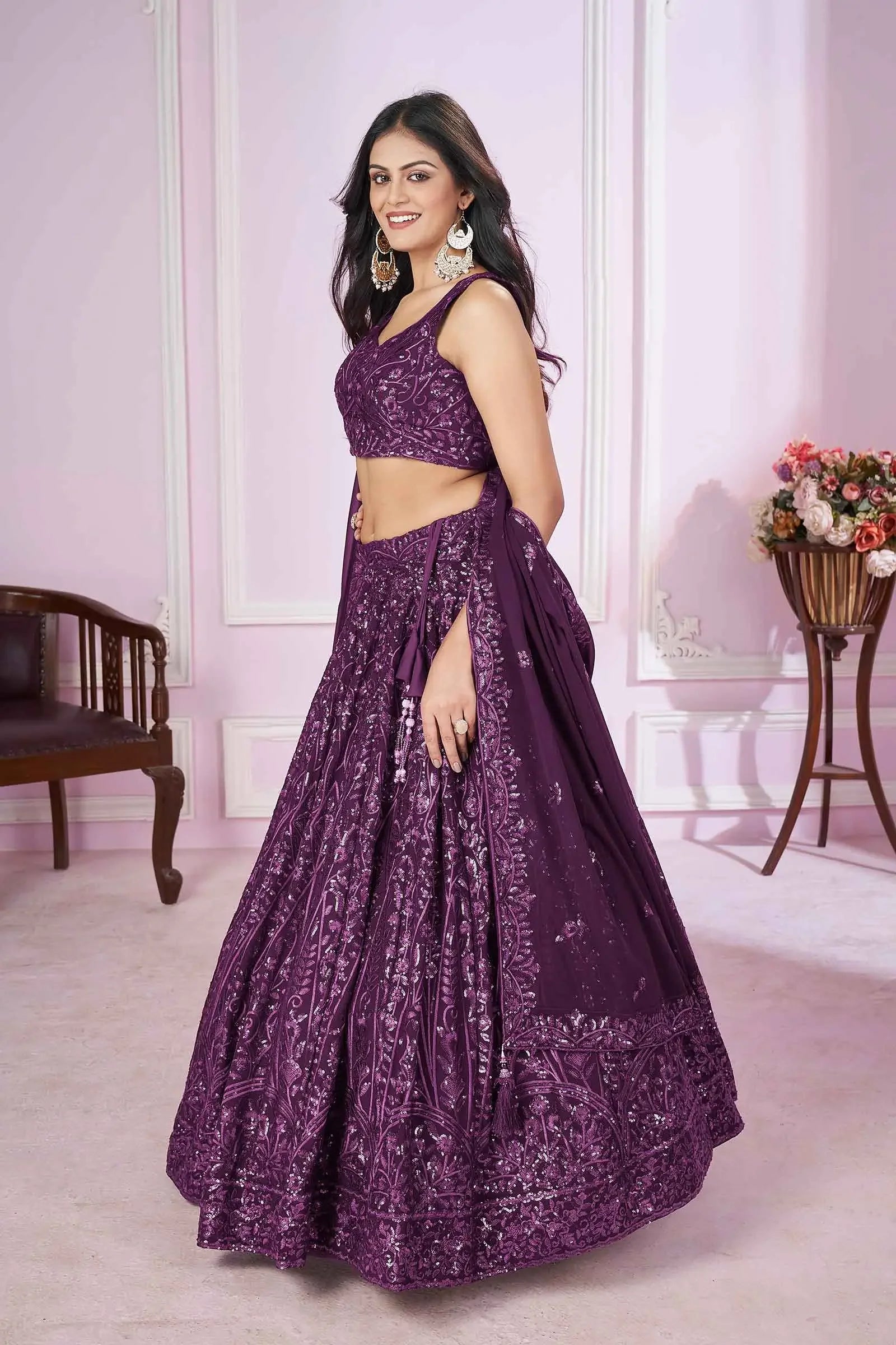 Woman wearing a purple embroidered lehenga set with dupatta in a pastel room.