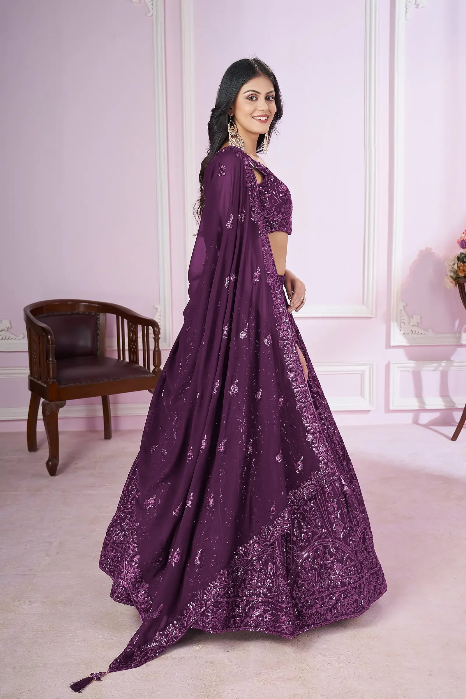 Woman in a purple embroidered lehenga with dupatta, standing in elegant room