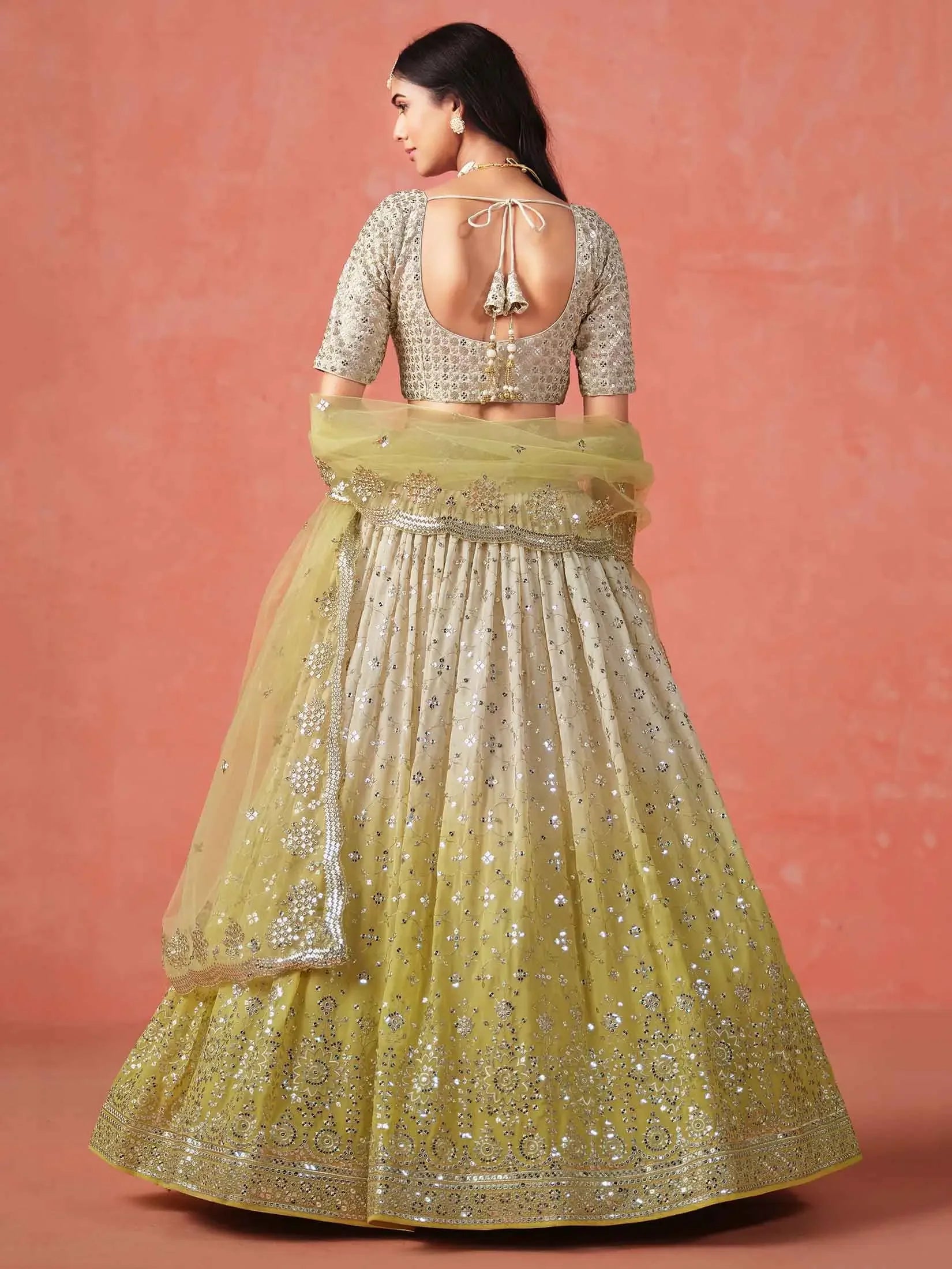 Woman wearing yellow sequin embroidered lehenga set with open-back blouse, traditional attire